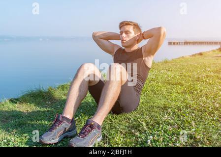 Giovane uomo sportivo che fa sit-up abs crunches in natura Foto Stock