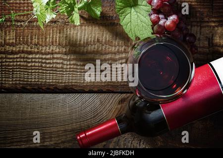 Vino rosso e uva. Vino rosso in un bicchiere, bottiglia, uva, foglie d'uva su un vecchio tavolo d'annata. Vista dall'alto. Foto Stock