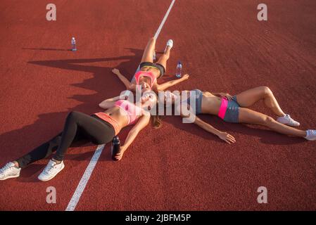 Fitness donne che riposano sul pavimento. Atleti stanchi che si trovano dopo un allenamento in palestra insieme in un cerchio in uno stadio Foto Stock