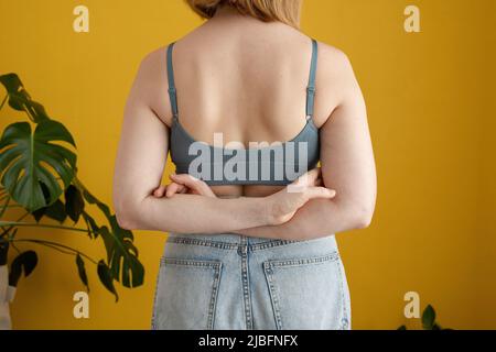 Vista posteriore di femmina ritagliata e irriconoscibile con capelli zenzero e corpo curvo in piedi contro il muro giallo a casa Foto Stock