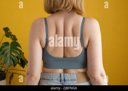 Vista posteriore di una donna irriconoscibile con capelli zenzero e corpo curvo in piedi contro il muro giallo in casa Foto Stock