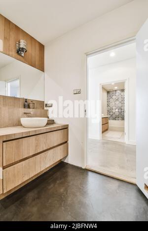 Interni simmetrici di bagno moderno con lavandino in ceramica su armadi in legno in appartamento contemporaneo Foto Stock