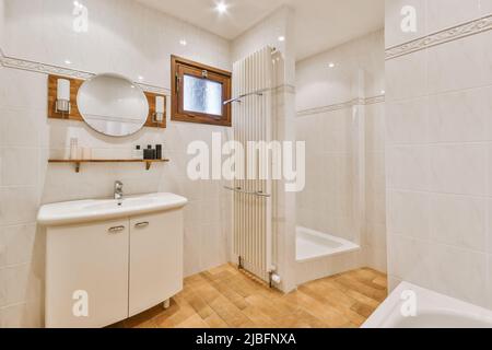 Lavandino in ceramica bianca con vasca e cabina doccia in bagno contemporaneo con pareti piastrellate lucide e dettagli in legno Foto Stock