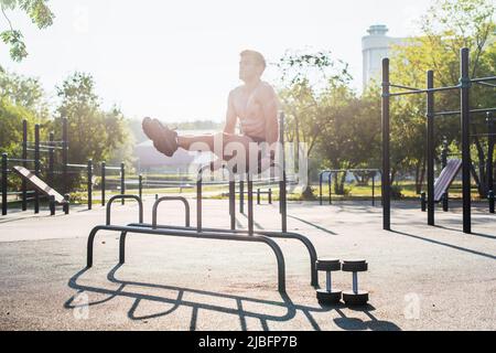 Giovane atleta forte allenarsi in palestra all'aperto, facendo gambe sollevamento abs esercizio Foto Stock
