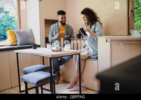 Coppia felice di fare colazione, seduta, riposo e parlare al coperto in una casa albero, routine mattina. Foto Stock
