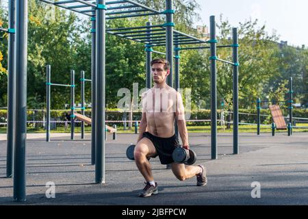 Giovane muscoloso fitness modello maschile facendo esercizi di affondo dumbbell nel parco Foto Stock