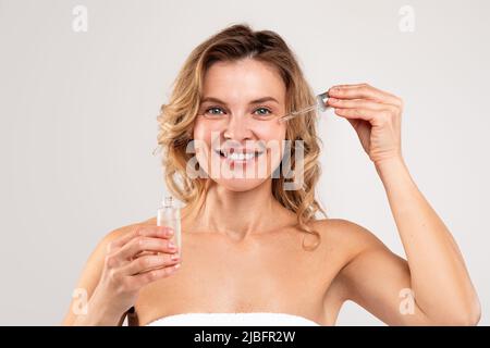 Cosmetici anti-età. Attraente Donna di mezza età applicando il siero della faccia sulla guancia Foto Stock