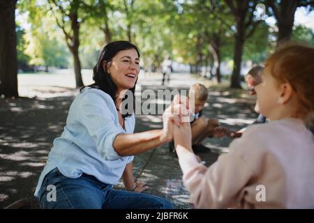 Coppia senior con nipote che disegnano con gessi su marciapiedi all'aperto nel parco. Foto Stock