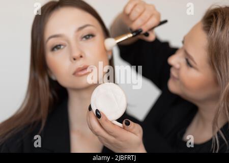 Donna sfocata viso spazzolando con pelle perfetta sana e brillante applicando la polvere naturale trucco sulle guance. Arrossire il tono della pelle Foto Stock