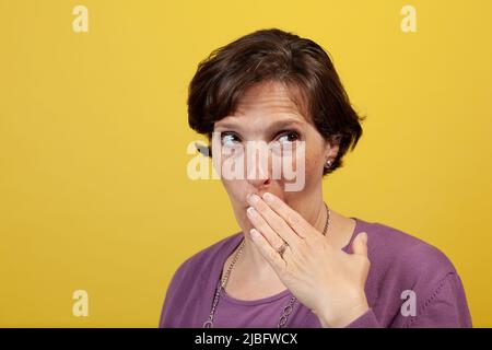 Donna matura attraente in blusa viola con mano sulla bocca che guarda via Foto Stock