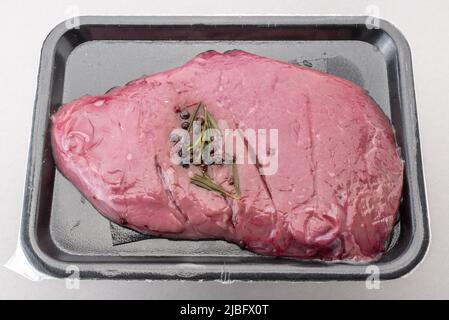 Bistecca di manzo con aromi su vassoio di plastica nero confezionato sottovuoto sigillato per la conservazione in frigorifero isolato su sfondo grigio Foto Stock