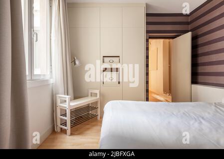 camera matrimoniale con armadi a muro, pareti con carta da parati decorativa a righe e armadio in legno per scarpe Foto Stock