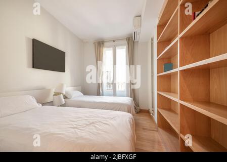 camera da letto con due piccoli letti bianchi, balcone con tende e ripiani in legno color ciliegia Foto Stock