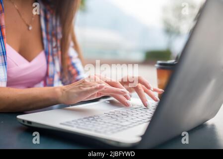 Primo piano di una digitazione femminile con le mani su una tastiera di un laptop. Giovane donna che studia e lavora nel parco. Foto Stock