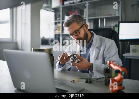 Ingegnere robotico che lavora alla desing di un moderno braccio robotico seduto al dest in laboratorio. Foto Stock