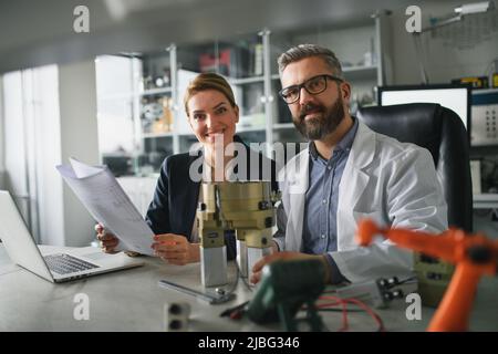 Ingegneri robotici che lavorano su computer portatili e desingendo un moderno braccio robotico in laboratorio. Foto Stock