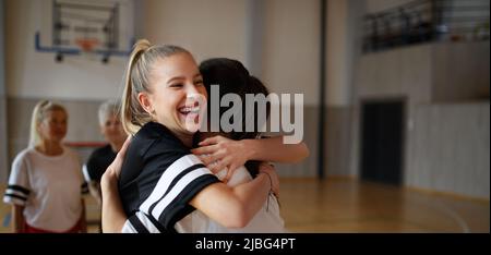 Gruppo di donne giovani e anziane, giocatori di squadra sportiva, in palestra festeggia la vittoria, abbraccia. Foto Stock