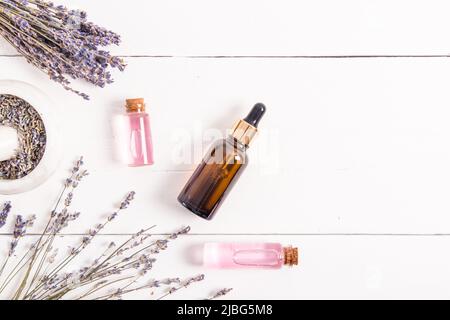 composizione di prodotti cosmetici naturali di fiori e semi di lavanda. siero o olio in bottiglie di vetro su sfondo bianco di legno. vista dall'alto Foto Stock