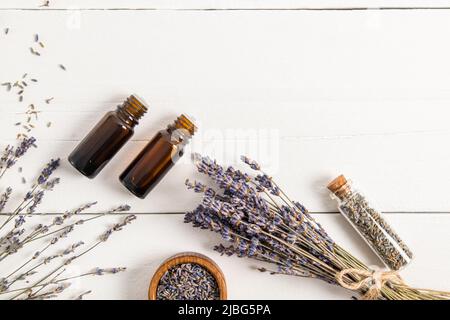 due bottiglie di vetro scuro con olio essenziale di lavanda, un bouquet di lavanda secca e semi su un tavolo bianco del villaggio. vista dall'alto, una copia dello spazio Foto Stock