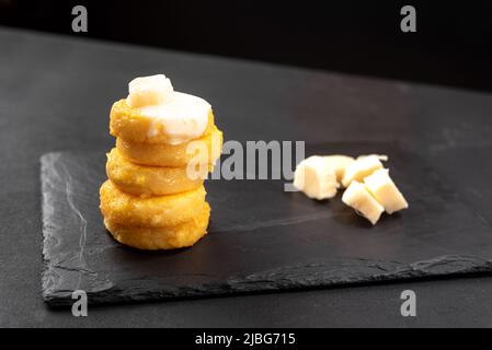 Una pila di dischi di Polenta fritta, spazio per copiare il testo su sfondo scuro con formaggio a base di matzarella Foto Stock