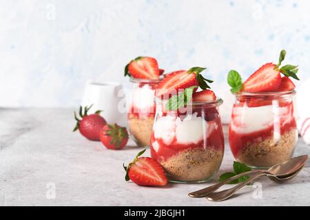 Cheesecake alla fragola. Cheesecake o trifle con fragola in vetro su sfondo vecchio tavolo grigio cemento. Cheesecake senza cottura. Dess Foto Stock