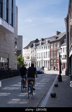 Due ciclisti vanno dalla 'Gubbelstraat' alla 'Markt' nella città olandese di Maastricht in una giornata di sole. Sulla sinistra il Mosae Forum con negozi Foto Stock