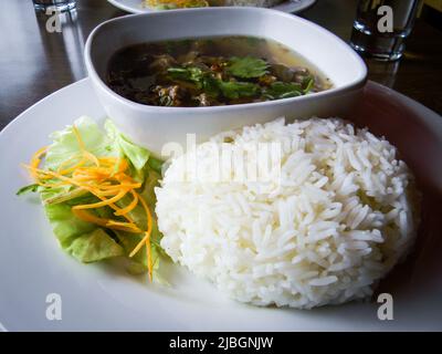 Nua Tun (tradizionale zuppa di manzo tailandese), riso Jasmine al vapore e insalata sul piatto nel ristorante. Foto Stock