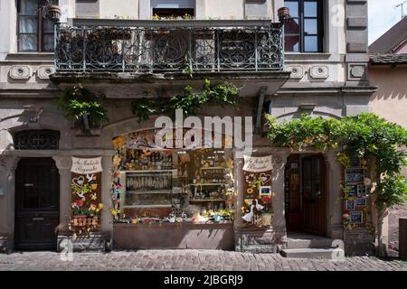 Vetrata riccamente decorata di un piccolo negozio 'Au Marché de Riquewihr' con un vecchio balcone sopra a Riquewihr in Alsazia, Francia Foto Stock