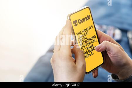 San Francisco, CA, Stati Uniti, maggio 2022: Donna che tiene un telefono con l'applicazione mobile Grindr sullo schermo. Sullo sfondo il logo Grindr si offuscava. Grindr è dati Foto Stock