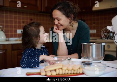 Madre amorevole e sua figlia carina che amano preparare il dessert Tiramisù italiano, insieme in lavoro di squadra, in cucina casalinga. Passatempo in famiglia, educazione culinaria Foto Stock