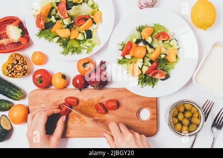 Le mani femminili fanno insalata greca, tagliano le verdure fresche, vista dall'alto sul tavolo da cucina con gli ingredienti Foto Stock