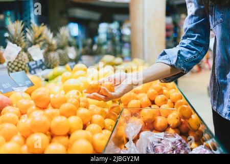 Selezione di tangerini in scaffale al supermercato, la mano della donna prende gli agrumi freschi di arancia, primo piano Foto Stock