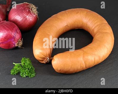 Anello bavarese di salsiccia di maiale in involucro naturale servito con cipolle rosse e prezzemolo su una tavola nera di ardesia Foto Stock