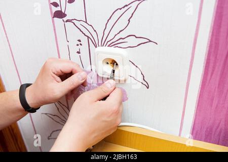 La spina e la presa sono bruciate, l'uomo sta tenendo una presa bruciata.cortocircuito, fuoco, pericolo. L'elettricista savvita la presa e la sostituisce Foto Stock