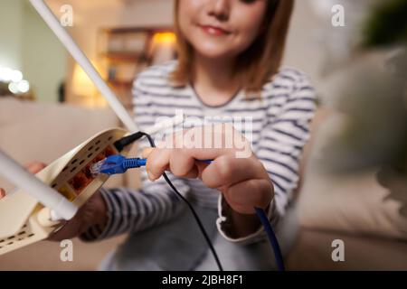 Immagine closeup della donna che collega il cavo Ethernet al retro del modem per ottenere una velocità più veloce Foto Stock