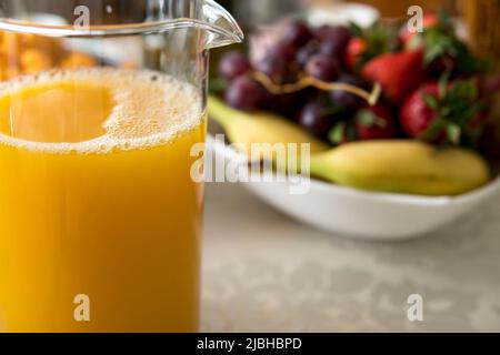 vaso di vetro con succo d'arancia davanti a un recipiente pieno di frutta Foto Stock