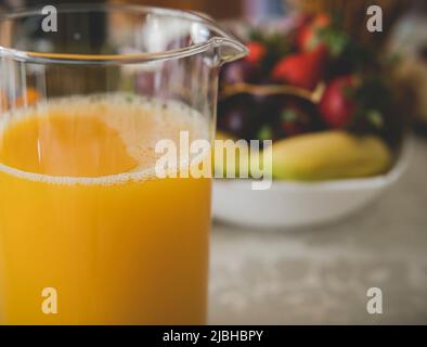 vaso di vetro con succo d'arancia davanti a un recipiente pieno di frutta Foto Stock