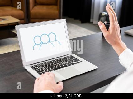 Conferenze virtuali. Uomo d'affari che accoglie i partner con la mano, parla tramite videochiamata, tiene incontri d'affari online. Concetto di lavoro remoto. Uomo seduto al tavolo con un computer portatile. Foto di alta qualità Foto Stock