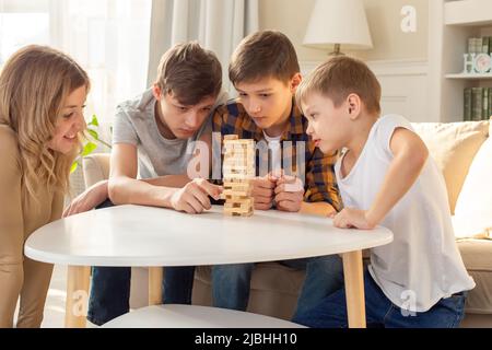 Una donna sorridente e tre ragazzi stanno giocando con entusiasmo un gioco da tavolo fatto di blocchi rettangolari di legno Foto Stock