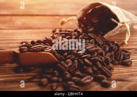 Primo piano dei chicchi di caffè tostati con anice in sacchetto di sacco su sfondo di legno il caffè è sempre una buona idea Foto Stock