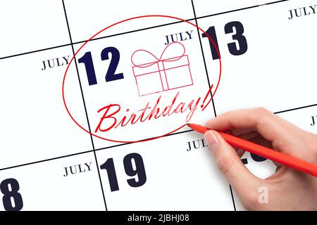 12th giorno di luglio. La mano cerchia la data sul calendario 12July, disegna una scatola regalo e scrive il testo compleanno. Vacanza. Mese d'estate, giorno del voi Foto Stock