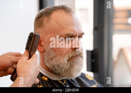 Un uomo anziano che intruda i capelli di un maestro in un barbiere. Un vecchio uomo ottiene un taglio di capelli elegante Foto Stock