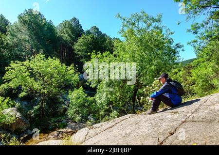 Uomo seduto su una grande roccia nel trekking in montagna, Guadarrama Madrid. Foto Stock