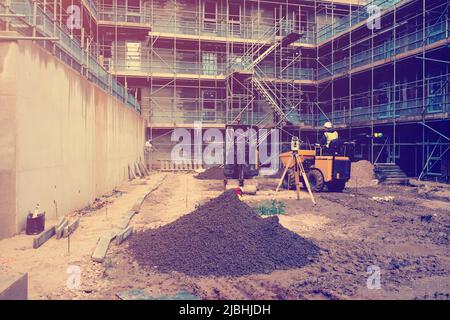 Costruttore che guida dumper e escavatore su un nuovo cantiere edile. Attrezzature di rilevamento sul cantiere Foto Stock