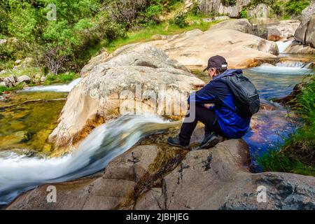 Uomo seduto su una roccia e guardando le cascate di acqua dolce che scende dalla montagna. Foto Stock