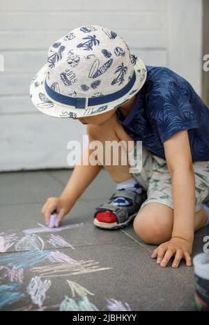 Piccolo ragazzo caucasico di tre anni seduto sul pavimento in cemento disegno con gesso in parco nella infanzia di giorno e crescere il concetto di istruzione Foto Stock