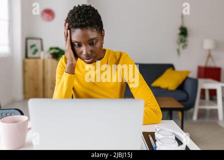 La giovane donna africana preoccupata che usa il portatile a casa Foto Stock