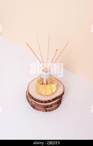 Bottiglia in vetro di diffusore di aroma su supporto in legno su sfondo bianco e beige neutro. Primo piano. Foto Stock