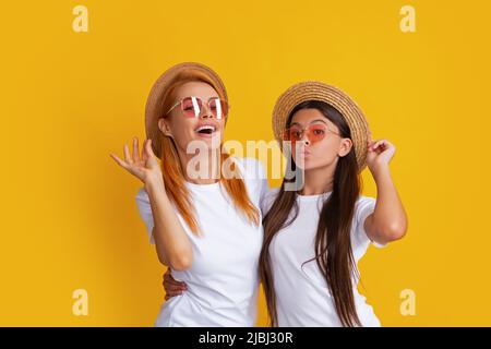 Studio ritratto di divertente bambino con mamma. Felice elegante madre e figlia in posa in studio su sfondo giallo, con cappello di paglia e occhiali da sole Foto Stock