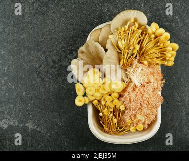 Una selezione di funghi culinari in un punnet dal mercato di un agricoltore su un piano di cucina in ardesia nera. Foto Stock